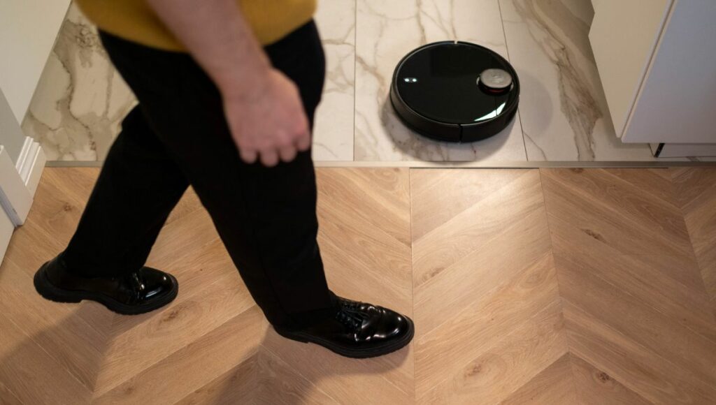 A man standing beside a robot vacuum